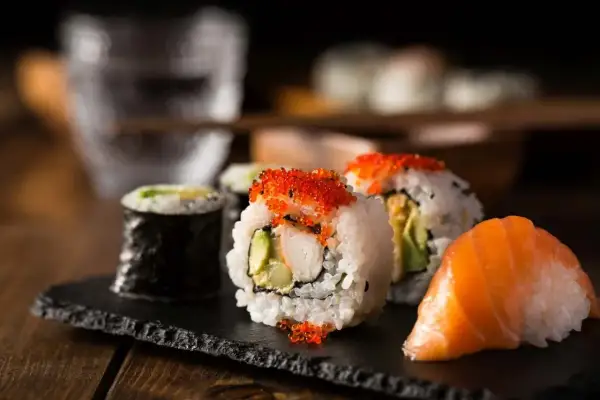 Sushi z łososiem, kawior i rolki z awokado na czarnej desce.